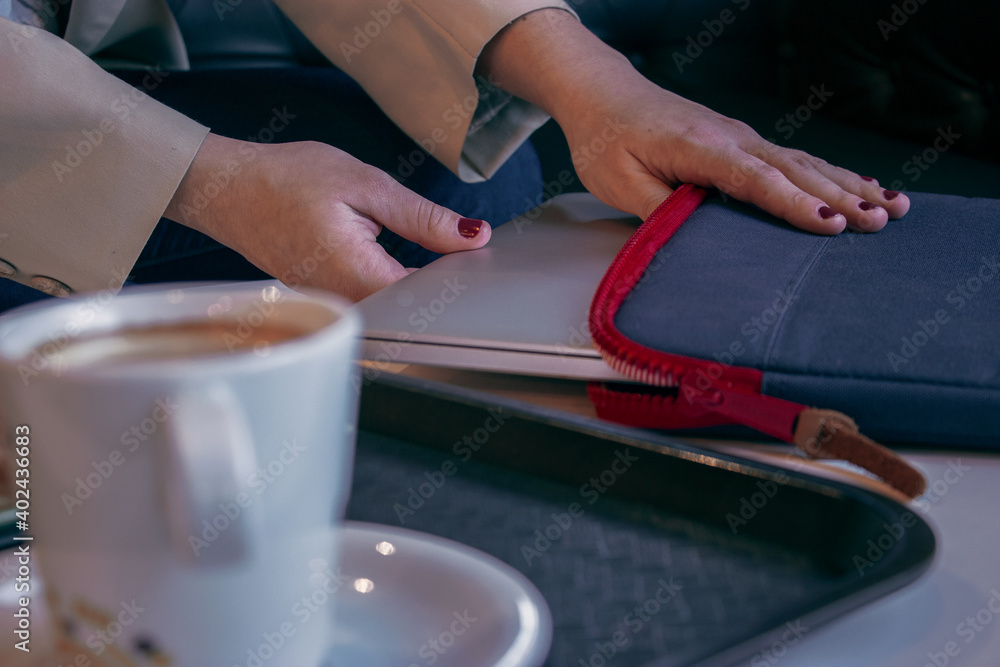 Girl takes her computer out of her bag to go to work while she has breakfast for the morning in a coffee shop. Girl Boss Concept 2021.