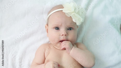 A little newborn girl lies on the bed and licks her fist. The baby looks into the camera. photo