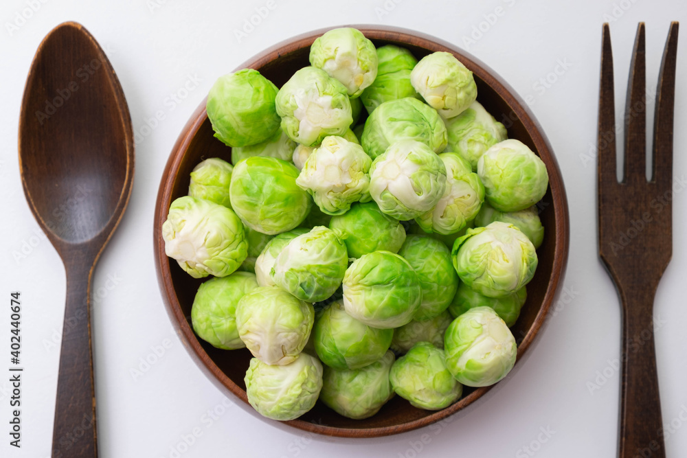 wooden fork and spoon on the table, between them green brussels sprouts in a wooden bowl wooden fork and spoon on the table, between them green brussels sprouts in a wooden bowl
