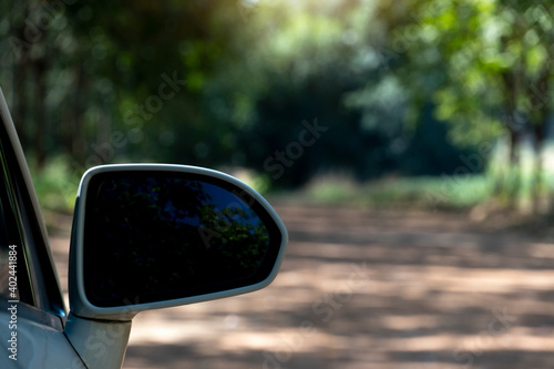 Close up wing mirror of white car stop on soil road with green forest at upcountry. 