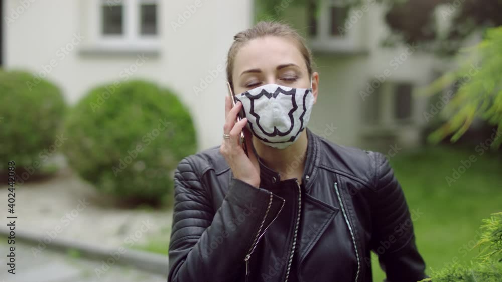 Young woman with ponytail hair in the colorfull cloth mask is picking up the phone and starts to talk. Young woman with ponytail hair in the colorfull cloth mask is picking up the phone and starts to talk.