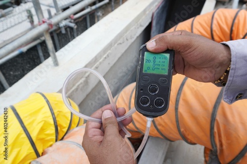 Construction supervisor hand holding gas detector device while commencing safety gas testing atmosphere at manhole to work construction site