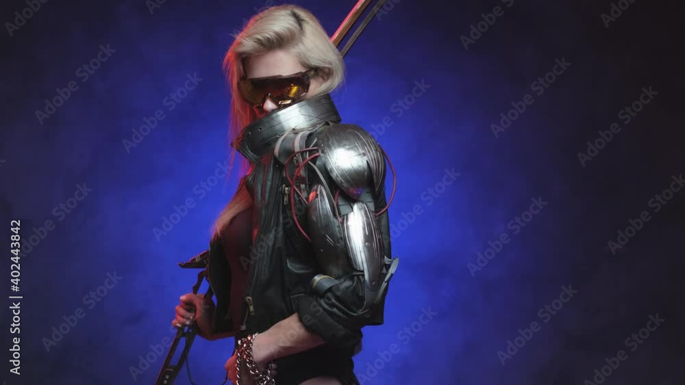 Futuristic cyber woman weared with eyewear poses in dark blue background holding a sword on her shoulder looking at camera. Feminine authority and fantasy portrait of a futuristic warrior. Futuristic cyber woman weared with eyewear poses in dark blue background holding a sword on her shoulder looking at camera. Feminine authority and fantasy portrait of a futuristic warrior.