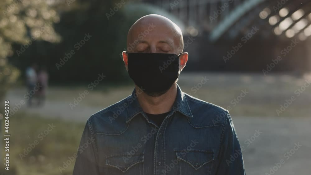 Face of a bald man in the park. He is wearing black mask and he is closing his eyes. Face of a bald man in the park. He is wearing black mask and he is closing his eyes.