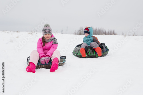 A girl and a boy are sitting on cheesecakes for rolling down a slide. Selective focus on a girl in a pink jacket. Walking in a deserted place.