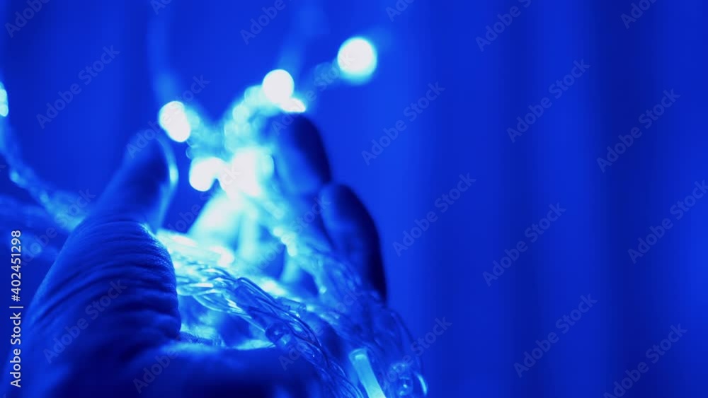 Female Hand Holds Christmas Twinkling Garland in Soft Defocus. 4K. Female Hand Holds Christmas Twinkling Garland in Soft Defocus. 4K.