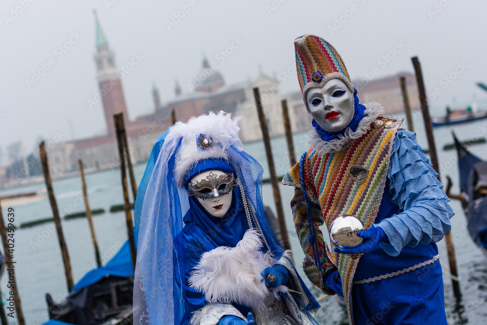 Obraz premium Venice, Italy - February 18, 2020: An unidentified couple in a carnival costume in front of a group of gondolas and St Giorgio's Island, attends at the Carnival of Venice.