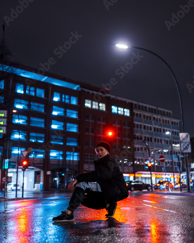 Woman posing on urban street in front of red street light at night