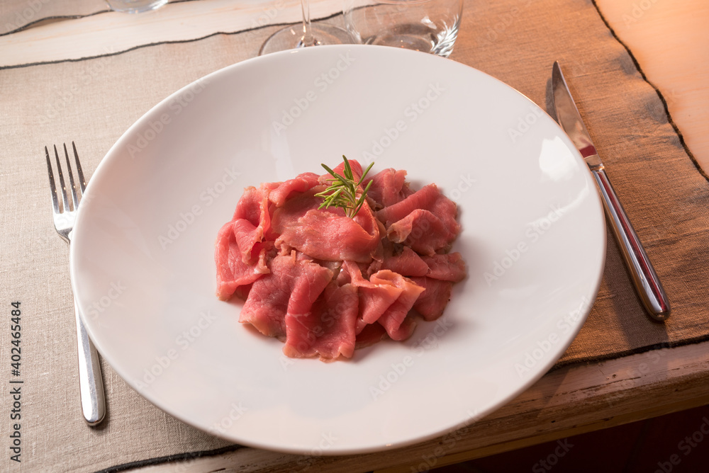 Beef carpaccio with rosemary on a table in a typical Piedmontese trattoria, Alba, Italy Beef carpaccio with rosemary on a table in a typical Piedmontese trattoria, Alba, Italy