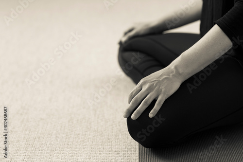 Horizontal side closeup of lower body of yogini on the floor with legs crossed in lotus pose. Woman indoors wearing black yoga pants with hands resting on knees. Home yoga practice in sepia tone