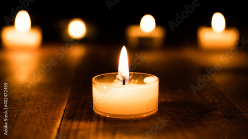 Burning candle light closeup in the dark. Beautiful bokeh and tealight atmosphere glowing at night background. Christian faith and hope concept