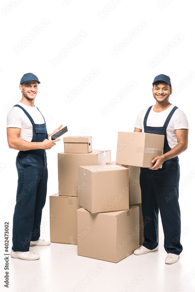 full length of cheerful worker holding digital tablet and standing with indian mover near boxes on white full length of cheerful worker holding digital tablet and standing with indian mover near boxes on white