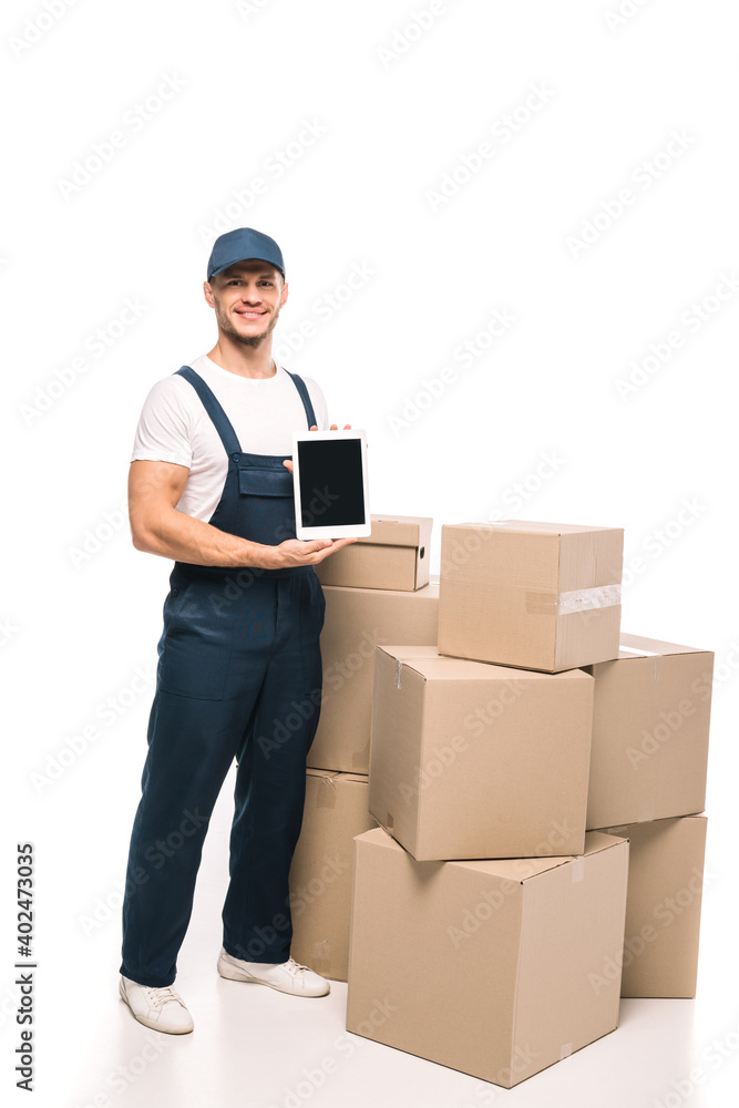 full length of cheerful mover in uniform and cap holding digital tablet with blank screen near carton boxes on white full length of cheerful mover in uniform and cap holding digital tablet with blank screen near carton boxes on white
