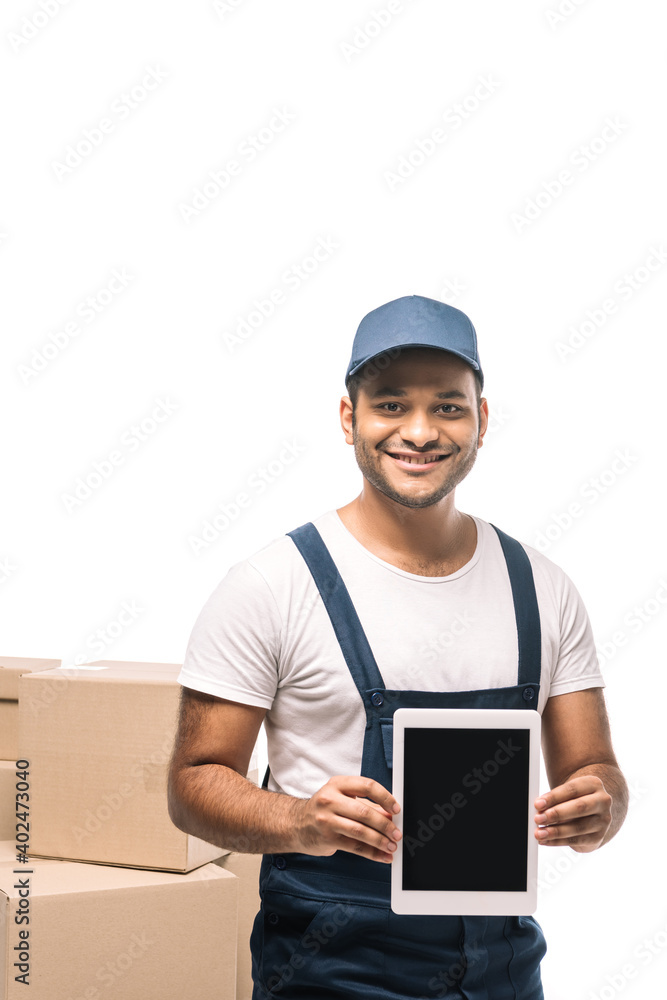 happy indian mover in overalls holding digital tablet with blank screen near carton boxes isolated on white happy indian mover in overalls holding digital tablet with blank screen near carton boxes isolated on white