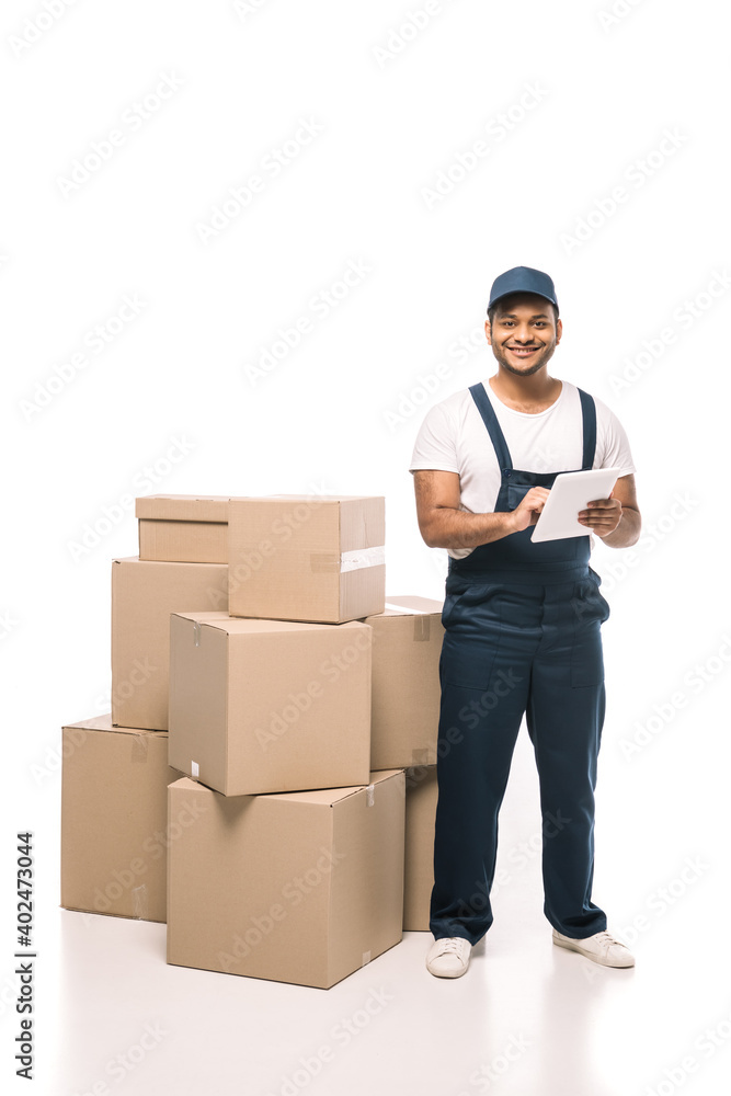 cheerful indian mover in overalls using digital tablet near carton boxes on white cheerful indian mover in overalls using digital tablet near carton boxes on white