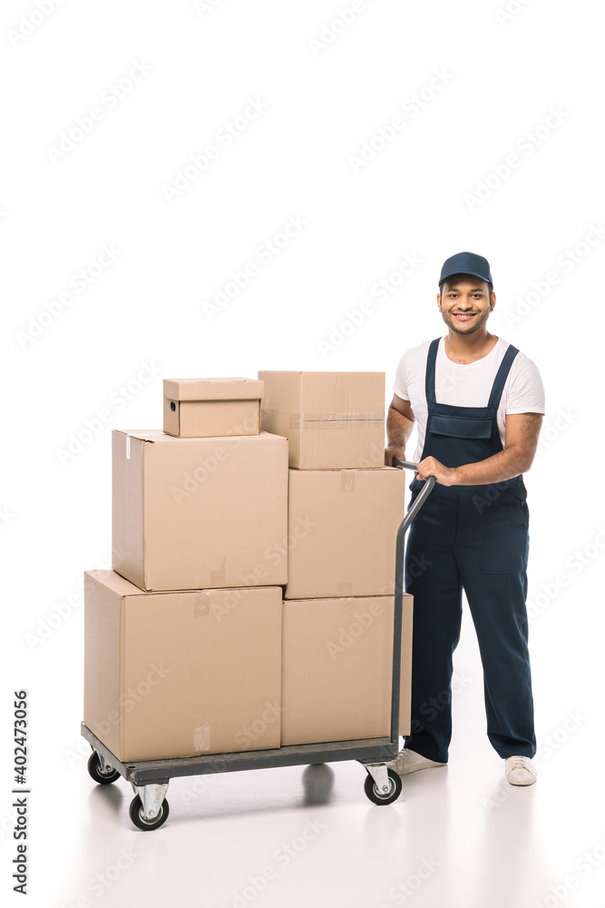 full length of happy indian mover in overalls standing near hand truck with carton boxes on white full length of happy indian mover in overalls standing near hand truck with carton boxes on white