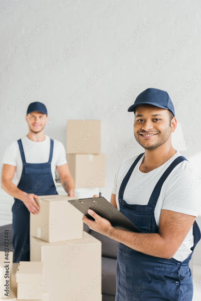 happy indian worker holding clipboard near coworker on blurred background happy indian worker holding clipboard near coworker on blurred background