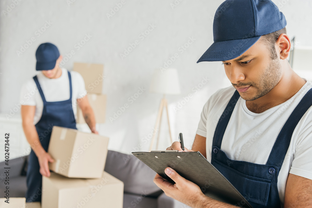 Indian worker writing on clipboard near coworker on blurred background Indian worker writing on clipboard near coworker on blurred background