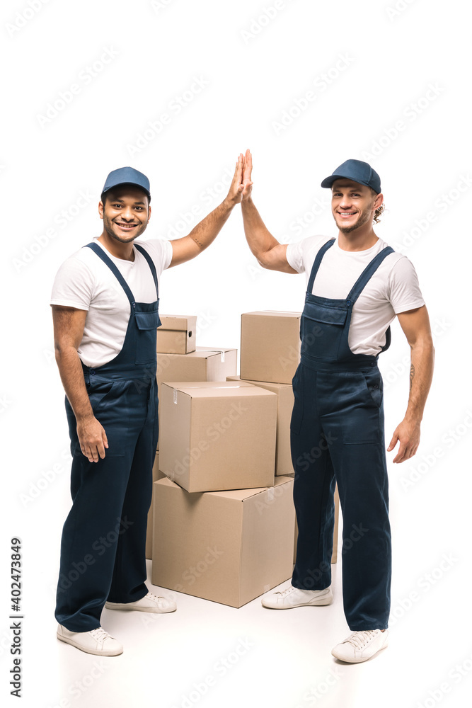 full length of happy multicultural workers giving high five near boxes on white full length of happy multicultural workers giving high five near boxes on white
