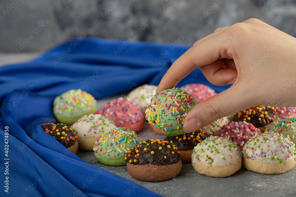 Woman hand taking colorful sweet small doughnut with sprinkles