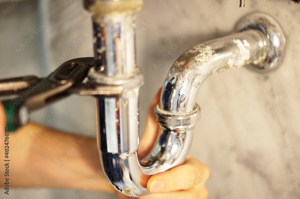 A close up of a hand holding a plumbing spanner screwing a fitting on wash basin waste pipe. A close up of a hand holding a plumbing spanner screwing a fitting on wash basin waste pipe.