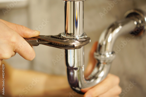 A close up of a hand holding a plumbing spanner screwing a fitting on wash basin waste pipe. 