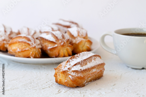 homemade vanilla eclairs or profiteroles on a plate on a white table. copy space. Traditional french tasty dessert and cup of black coffee on a background.