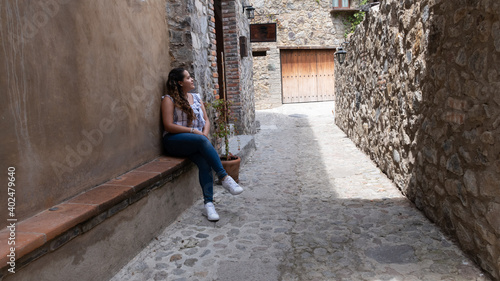 joven mujer blanca sentada en banca en calle rústica al fondo © Alfonso VargasTorres