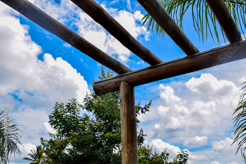 Pergolado de madeira, céu azul e vegetação tropical