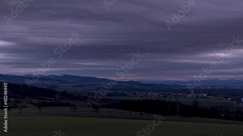 Timelapse view of a landscape with villages and the peaks of the Pustevny Mountains covered with snow in the background is a sunset and fast moving clouds across the sky.