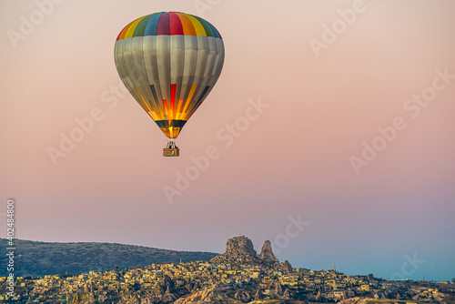 Hot air balloon rising in Cappadocia, Uchisar castle and city in the background, Early morning