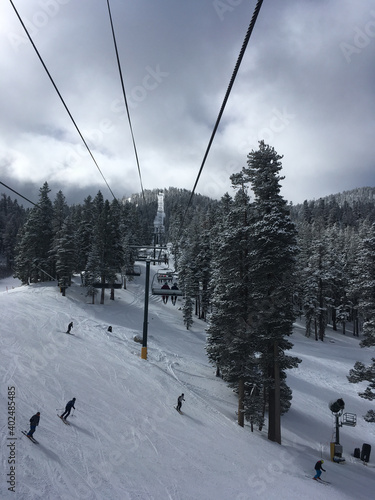 Moody winter scene at a ski resort on a grey and cloudy day, with a view of the chair lift, skiers and snow covered trees