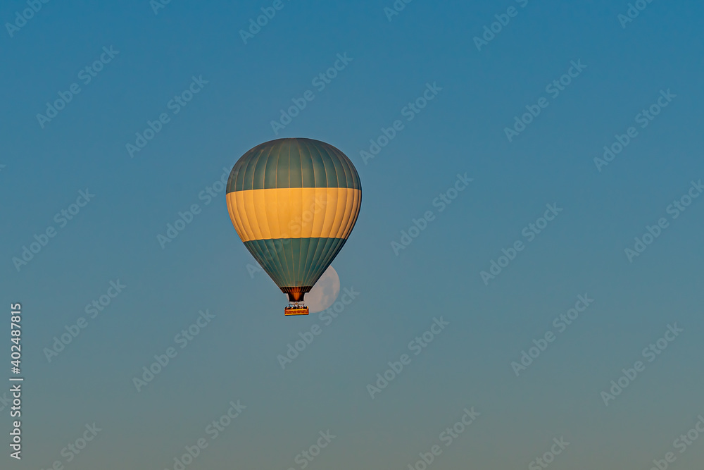 Fototapeta premium Hot air balloon flying over Cappadocia with full moon, blue sky