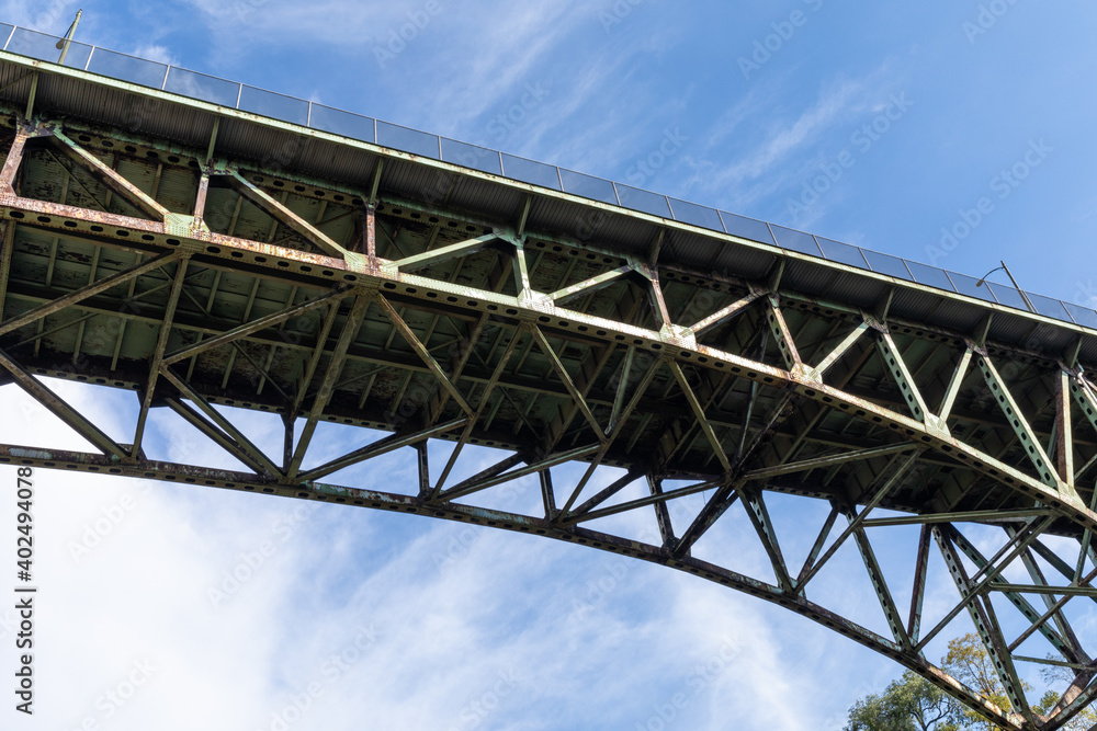 Arch bridge seen from below, rusting metal trusswork, blue sky with white clouds, horizontal aspect Arch bridge seen from below, rusting metal trusswork, blue sky with white clouds, horizontal aspect