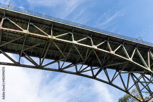 Arch bridge seen from below, rusting metal trusswork, blue sky with white clouds, horizontal aspect