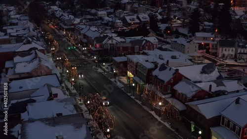 Cars, trucks, traffic on street through town at night. Christmas lights and snow covered rooftops in winter. Aerial drone view in Ephrata, PA, USA.