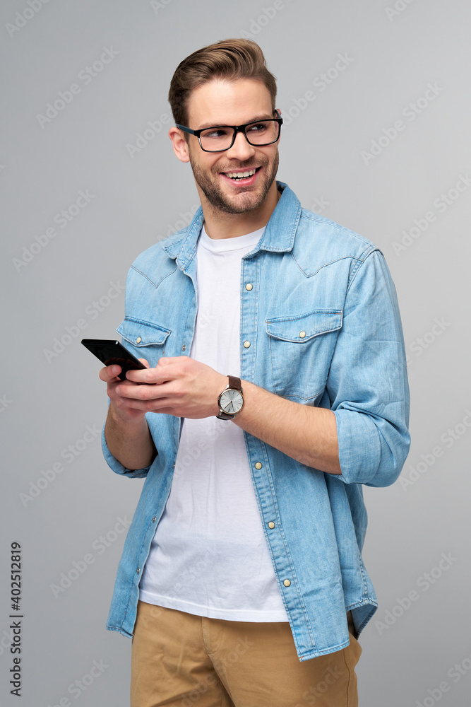 pretty casual man in blue jeans shirt holding his phone standing over studio grey background