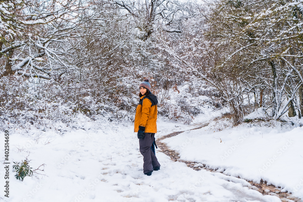 A young woman in a yellow jacket walking along the path of frozen trees. Snow in the town of Opakua near Vitoria in Araba, Basque Country. Spain
