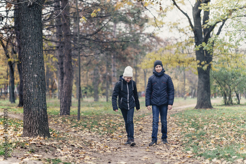 teen girl and boy walking through the park and enjoys autumn, beautiful nature with yellow leaves