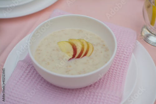 Oatmeal with apple for breakfast. Healthy eating. A useful breakfast. Porridge in a white ceramic cup on a pink tablecloth.