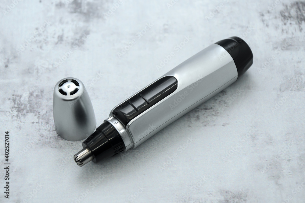 Compact electric nose and ear hair trimmer with cap on gray background. Removal unwanted hair of nose, ear and facial. Trim edge of beard, mustache, eyebrows. Compact electric nose and ear hair trimmer with cap on gray background. Removal unwanted hair of nose, ear and facial. Trim edge of beard, mustache, eyebrows.