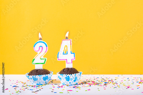 24 number candle on a cup cake with colorful sprinkles and yellow background twenty fourth birthday anniversary celebrations photo