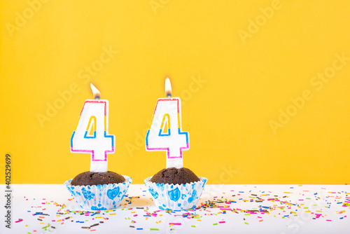 44 number candle on a cup cake with colorful sprinkles and yellow background forty fourth birthday anniversary celebrations photo