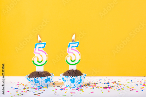 55 number candle on a cup cake with colorful sprinkles and yellow background fifty fifth birthday anniversary celebrations