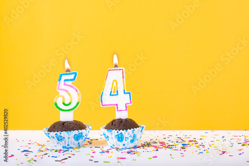 54 number candle on a cup cake with colorful sprinkles and yellow background fifty fourth birthday anniversary celebrations. photo