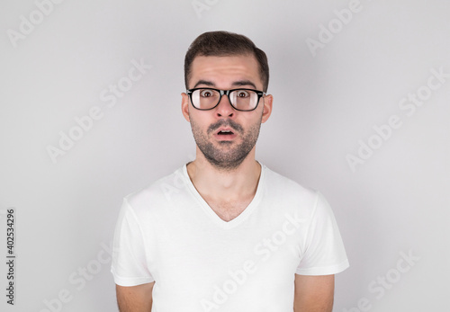Surprised man in eyeglasses wearing white undershirt over grey background © MP Studio