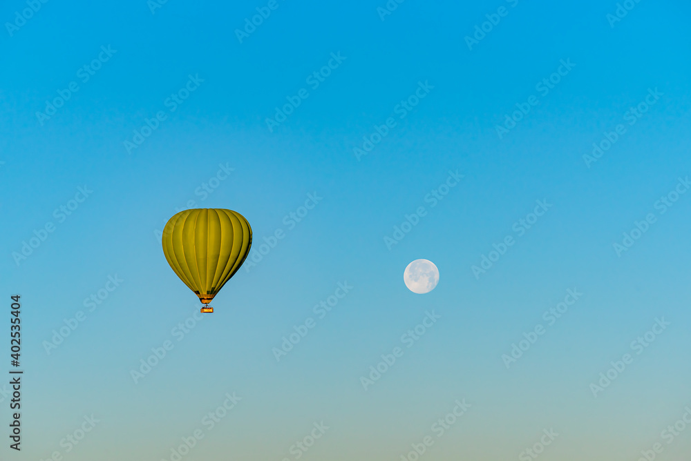 Fototapeta premium Hot air balloon flying over Cappadocia with full moon, in blue sky