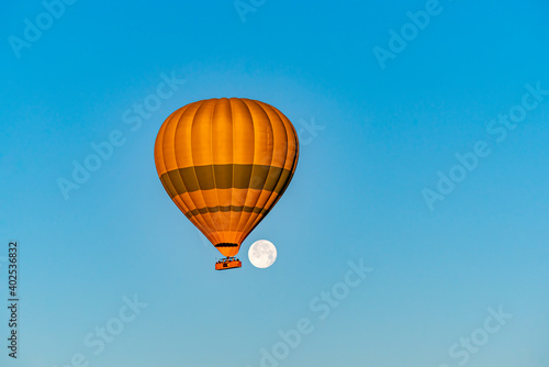 Hot air balloon flying over Cappadocia with full moon, in blue sky © attraction art