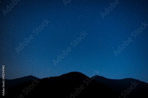 Silhouette of mountain range under dark blue night sky with many bright stars