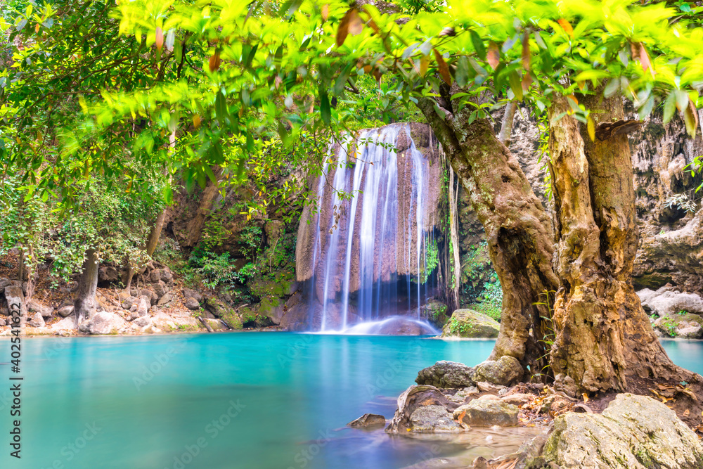 Beautiful waterfall in tropical jungle forest with big green tree and emerald lake on foreground. Nature landscape of Erawan National park, Kanchanaburi, Thailand